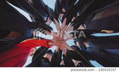 Group of graduates in academic gowns holding hands in a circle, representing unity and achievement Group of graduates in academic gowns holding hands in a circle, representing unity and achievement 140410197