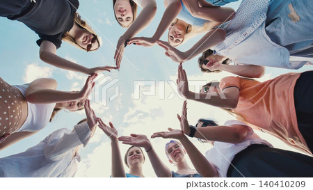 Group of school friends joining hands forming a star shape, symbolizing unity, teamwork, and friendship, against a bright blue sky Group of school friends joining hands forming a star shape, symbolizing unity, teamwork, and friendship, against a bright blue sky 140410209
