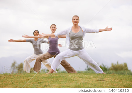 Group, yoga and women in warrior pose outdoor for healthy body, exercise and fitness. Park, virabhadrasana and people in nature for balance, stretching and friends practice together for wellness 140410210