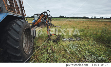 Tractor with rotary mower cutting grass in field on cloudy summer day 140410326