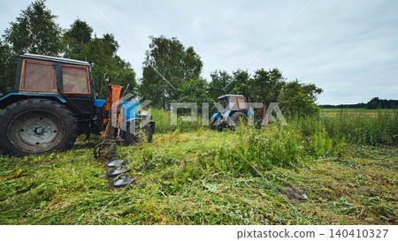 Tractors mowing grass in a field with rotary mowers 140410327