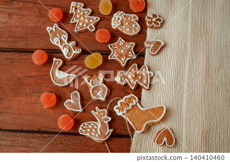 Decorated gingerbread pieces with icing details are spread across textured wood. Bright details create cheerful holiday atmosphere. 140410460