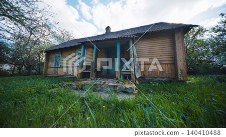 Abandoned old wooden house with porch on overgrown green grass in rural scene Abandoned old wooden house with porch on overgrown green grass in rural scene 140410488