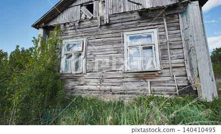 Abandoned old wooden rural house decaying in overgrown grass under blue sky Abandoned old wooden rural house decaying in overgrown grass under blue sky 140410495