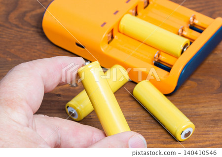 Four batteries held in a hand, with a charger in the background. Four batteries held in a hand, with a charger in the background. 140410546