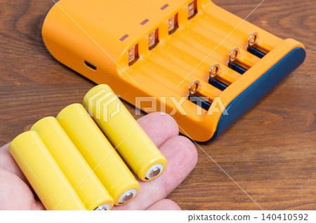 Four batteries held in a hand, with a charger in the background. Four batteries held in a hand, with a charger in the background. 140410592
