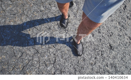 A man walks through mud and swampy cracked earth. A man walks through mud and swampy cracked earth. 140410634
