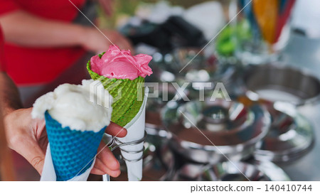 Hand holding colorful ice cream cones getting a refreshingly sweet dessert Hand holding colorful ice cream cones getting a refreshingly sweet dessert 140410744