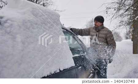 Man cleaning heavy snow from car during blizzard, winter driving challenges Man cleaning heavy snow from car during blizzard, winter driving challenges 140410749