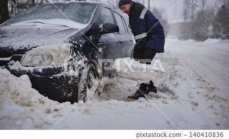 Man shoveling snow from stuck car during a heavy blizzard and winter storm Man shoveling snow from stuck car during a heavy blizzard and winter storm 140410836