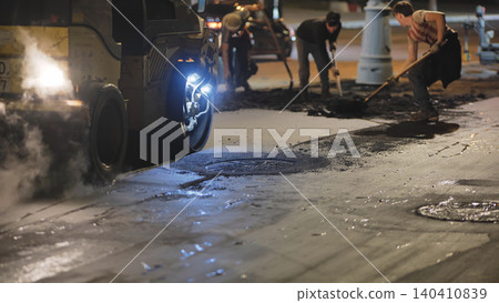 Road roller compacting fresh asphalt during night street construction with workers Road roller compacting fresh asphalt during night street construction with workers 140410839
