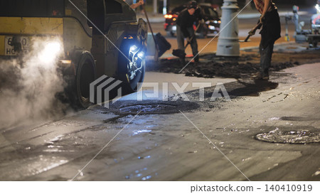 Road worker operating asphalt paver at night rebuilding city street Road worker operating asphalt paver at night rebuilding city street 140410919