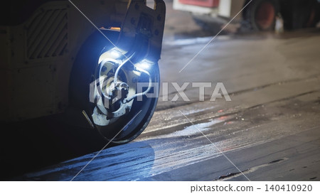 Road roller compacting fresh asphalt paving infrastructure at construction site night 140410920