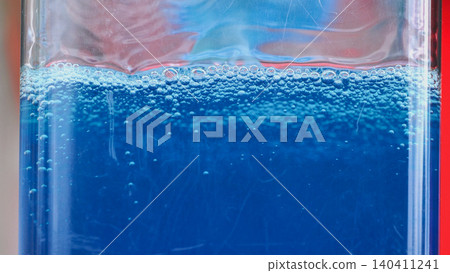 Blue liquid creating a foamy surface with many small bubbles inside a glass container 140411241
