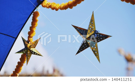 Golden stars and yellow garlands hanging against blue sky in India Golden stars and yellow garlands hanging against blue sky in India 140411251