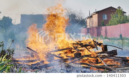 Backyard fire burning wood and debris in residential area. Intense flames and smoke rising 140411303