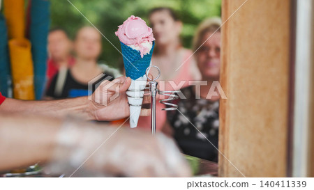 Vendor handing strawberry and vanilla ice cream in a blue waffle cone to a customer Vendor handing strawberry and vanilla ice cream in a blue waffle cone to a customer 140411339