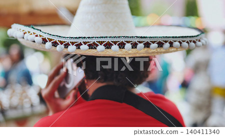 Person wearing a traditional sombrero using smartphone during Mexican festival Person wearing a traditional sombrero using smartphone during Mexican festival 140411340