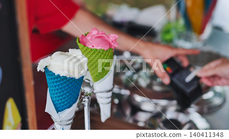 Customer paying for colorful ice cream cones with a credit card at a street food stall Customer paying for colorful ice cream cones with a credit card at a street food stall 140411348