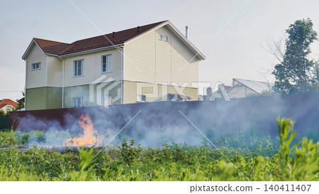 Fire burning uncontrollably near a residential house producing smoke Fire burning uncontrollably near a residential house producing smoke 140411407