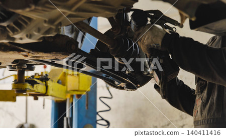 Mechanic repairing car chassis lifted on a hydraulic ramp Mechanic repairing car chassis lifted on a hydraulic ramp 140411416