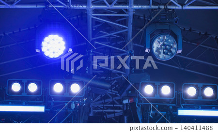 Concert stage lighting equipment shining blue spotlights on truss structure 140411488
