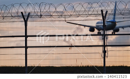 Airport fence with barbed wire and approaching airplane at sunset Airport fence with barbed wire and approaching airplane at sunset 140411523
