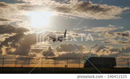 Passenger airplane landing at sunset in a cloudy sky over the airport fence Passenger airplane landing at sunset in a cloudy sky over the airport fence 140411525