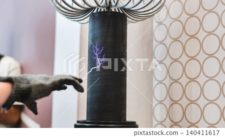 Hand in protective glove touching Tesla coil creating an electric arc discharge Hand in protective glove touching Tesla coil creating an electric arc discharge 140411617