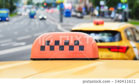 Taxi cab roof sign with checkered pattern on a city street, urban traffic moving Taxi cab roof sign with checkered pattern on a city street, urban traffic moving 140411621