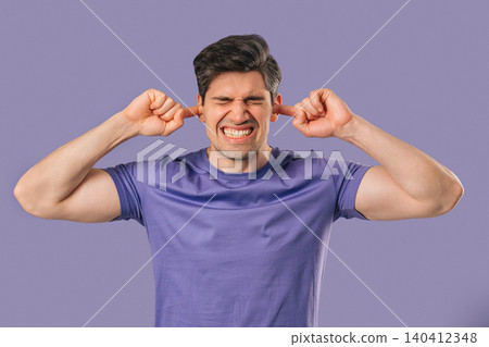 Young man Covering Ears, Showing Irritation In Violet Studio. Stress, Overload Young man Covering Ears, Showing Irritation In Violet Studio. Stress, Overload 140412348