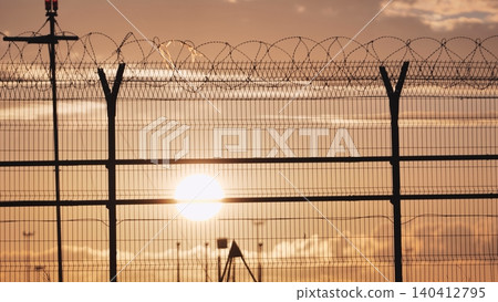 Airport security fence with barbed wire at sunset, protecting restricted area Airport security fence with barbed wire at sunset, protecting restricted area 140412795