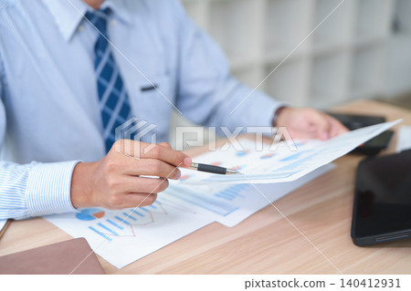 Business professional analyzing financial reports and charts at desk with documents Business professional analyzing financial reports and charts at desk with documents 140412931