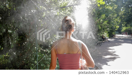 Young woman cooling down with water mist spray in park Young woman cooling down with water mist spray in park 140412963