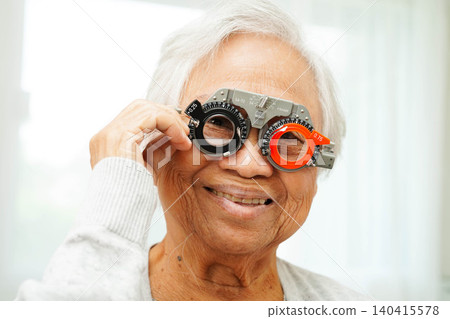 Optometrist checking Asian elderly woman ophthalmic vision eye test and using optical trial frame. 140415578