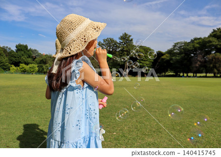 A girl's back as she enjoys playing with soap bubbles in a summer park. A girl's back as she enjoys playing with soap bubbles in a summer park. 140415745