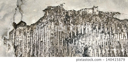 The texture of an old concrete wall with peeling plaster, revealing the rough surface beneath. 140415879