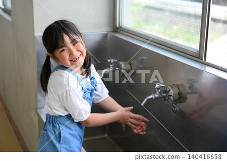 A female elementary school student smiles as she washes her hands at the school's handwashing area. A female elementary school student smiles as she washes her hands at the school's handwashing area. 140416858