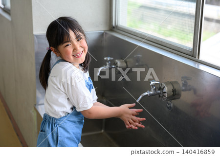 A female elementary school student smiles as she washes her hands at the school's handwashing area. A female elementary school student smiles as she washes her hands at the school's handwashing area. 140416859