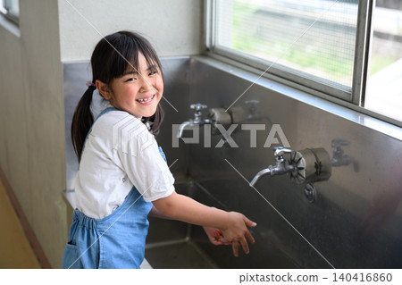 A female elementary school student smiles as she washes her hands at the school's handwashing area. A female elementary school student smiles as she washes her hands at the school's handwashing area. 140416860