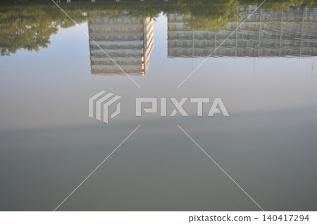 The city and the lush green landscape reflected on the calm surface of the water. 140417294
