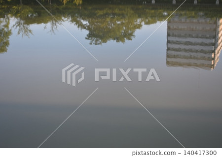 The city and the lush green landscape reflected on the calm surface of the water. 140417300
