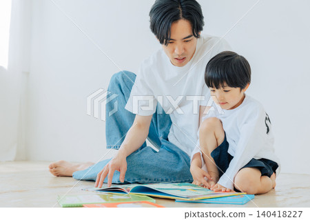 一個男孩正在和父親一起讀圖畫書。 140418227