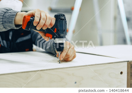 Person uses a drill to assemble furniture in a workshop during daylight hours Person uses a drill to assemble furniture in a workshop during daylight hours 140418644