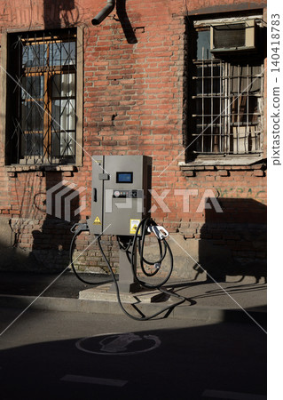 Outdoor EV charger on a city street curb in front of an aged red brick building with windows Outdoor EV charger on a city street curb in front of an aged red brick building with windows 140418783
