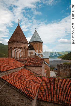 Medieval stone church domes and red tile roofs overlooking scenic Zhinvali Reservoir 140418785