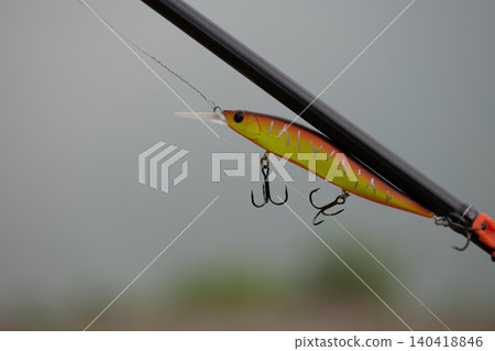 A fishing lure is attached to a fishing rod over calm water in the morning. A fishing lure is attached to a fishing rod over calm water in the morning. 140418846