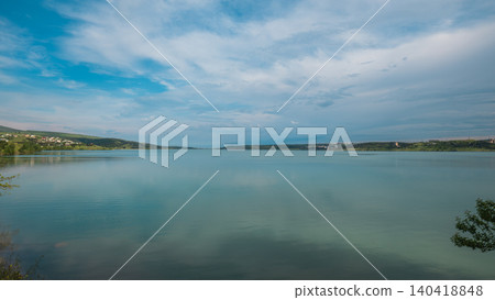 A lake reflects the sky and nearby hills during the day with clouds above A lake reflects the sky and nearby hills during the day with clouds above 140418848