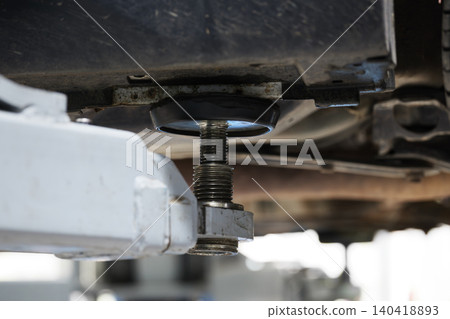 Detail view of a professional hydraulic lift arm supporting a car frame in a repair shop Detail view of a professional hydraulic lift arm supporting a car frame in a repair shop 140418893