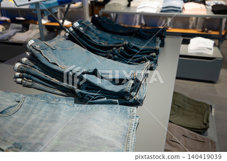 Close-up shot of folded blue denim trousers neatly stacked on a gray display table in a boutique Close-up shot of folded blue denim trousers neatly stacked on a gray display table in a boutique 140419039